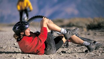 A young exercising woman has fallen off her mountain bike and holds her injured knee. accident, accidental, sport injury, bicycle